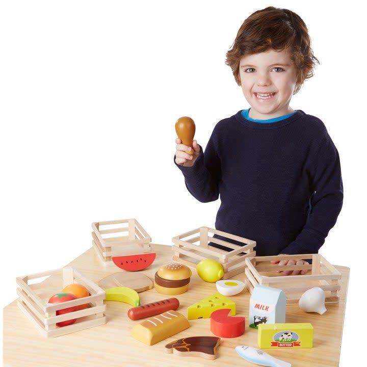 A kid holding a drumstick surrounded by play food