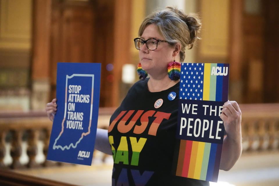 FILE - Kristen Cooper holds signs outside of the Senate chamber at the Indiana Statehouse, Wednesday, Feb. 22, 2023, in Indianapolis. Indiana Republican state Senators voted Tuesday, Feb. 28, to advance a ban on all gender-affirming care for those under 18, the latest in this year's conservative movement by states aiming to limit the rights of transgender youth. (AP Photo/Darron Cummings, File)