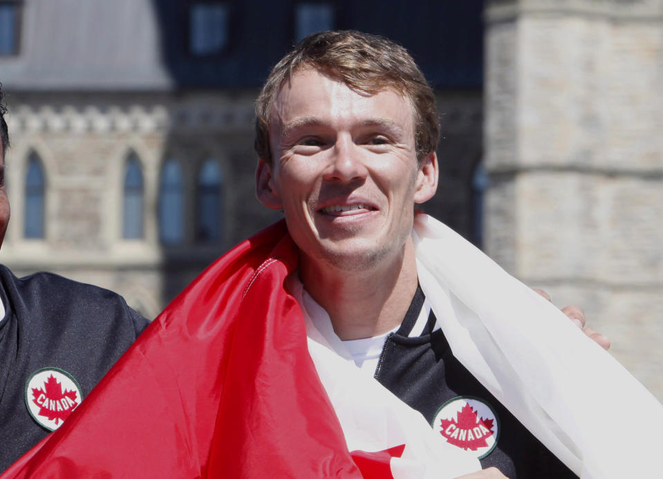 Triathlete Simon Whitfield is wrapped in the Canadian Flag after he was named the official flag bearer for Canada at the 2012 London Olympics, on Parliament Hill, Thursday July 12 2012 in Ottawa. THE CANADIAN PRESS/Fred Chartrand