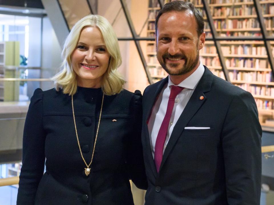 Norwegens Kronprinzessin Mette-Marit und Kronprinz Haakon arm in arm vor einer Bücherregal-Wand