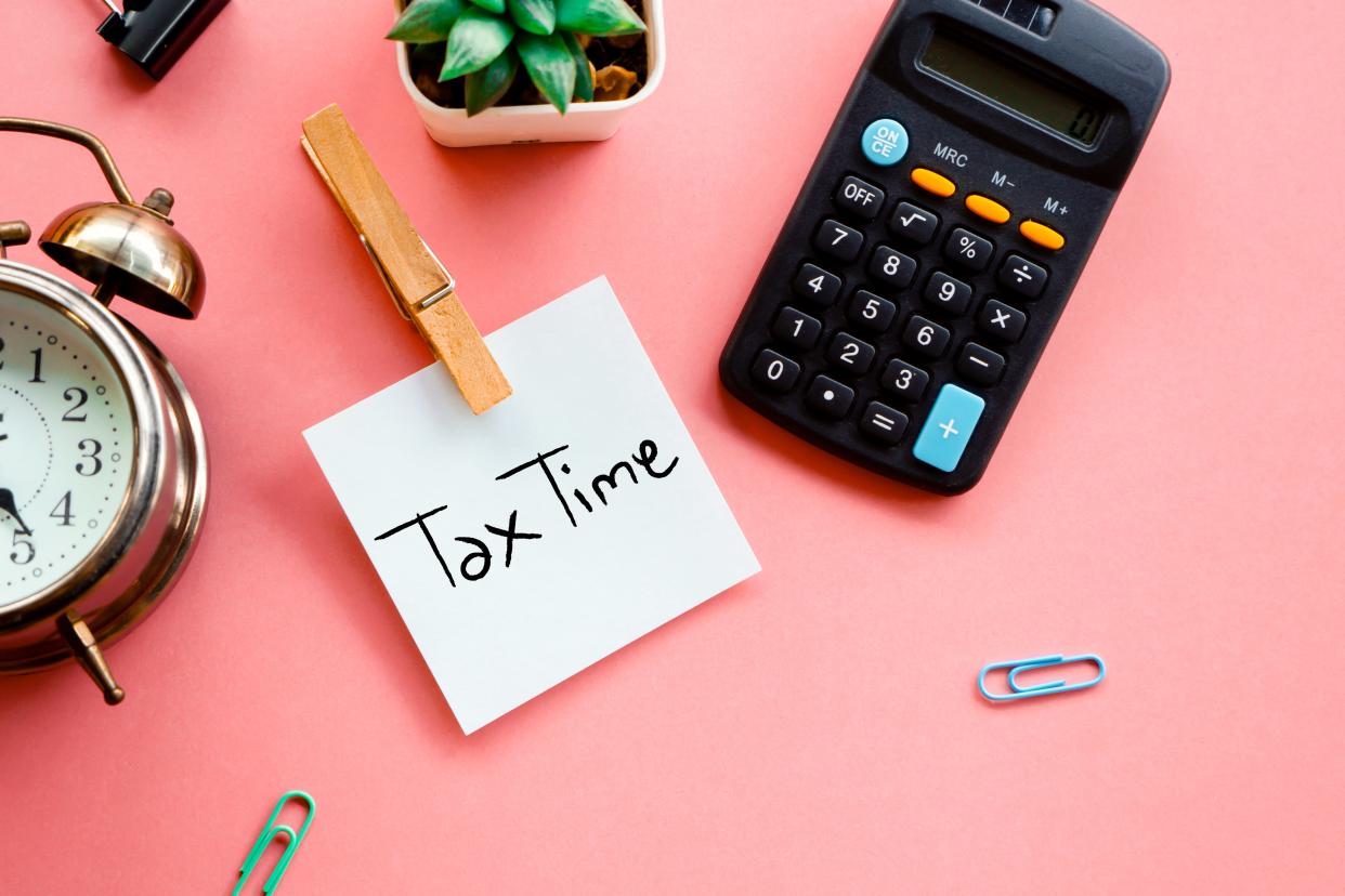 Tax time concept on a sticky note, calculator and clock on a pink background