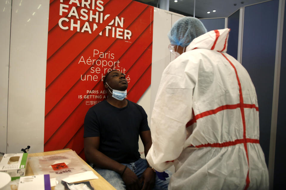 A health worker is going to collect a nasal swab sample for COVID-19 test, at the Roissy Charles de Gaulle airport, outside Paris, Saturday, Aug. 1, 2020. Travelers entering France from 16 countries where the coronavirus is circulating widely are having to undergo virus tests upon arrival at French airports and ports.(AP Photo/Thibault Camus)