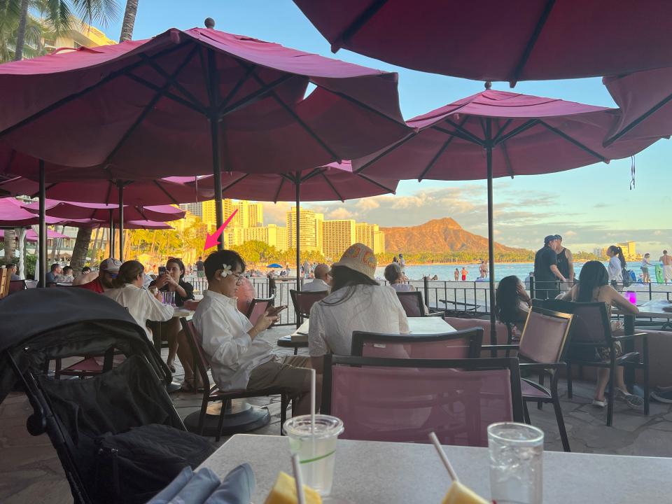 An arrow points to a person on the beach next to a crowded waterfront restaurant with drinks in view.