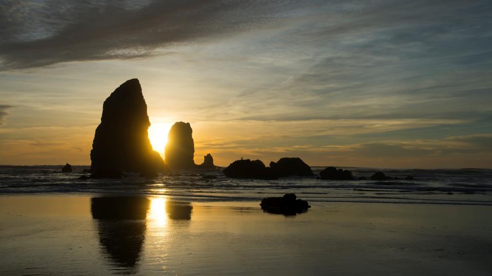 stacks of rocks reflecting in the sea below, the sun is setting in the distance.