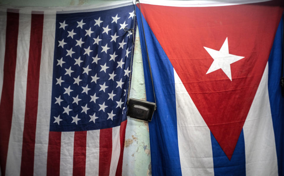 A U.S. and Cuban flags hang from a wall with an old photo camera hung in between in Havana, Cuba, Monday, Jan 11, 2021. The Trump administration has re-designated Cuba as a "state sponsor of terrorism" in a move that hits the country with new sanctions shortly before President-elect Joe Biden takes office. (AP Photo/Ramon Espinosa)