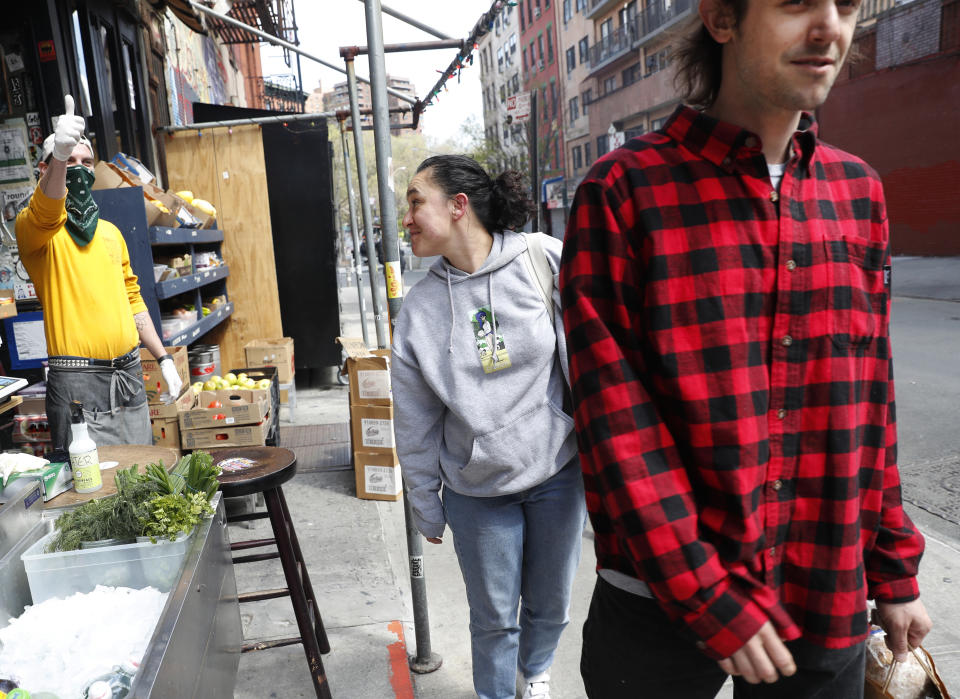 Managing partner Derek Tigue, left, gives a thumbs-up sign to a friend as customers leave the FMN General Store with groceries after shopping at the former Forgtmenot bar during the coronavirus outbreak, Wednesday, April 15, 2020, in New York. Tigue's partners and friends converted the bar into a grocery store. (AP Photo/Kathy Willens)