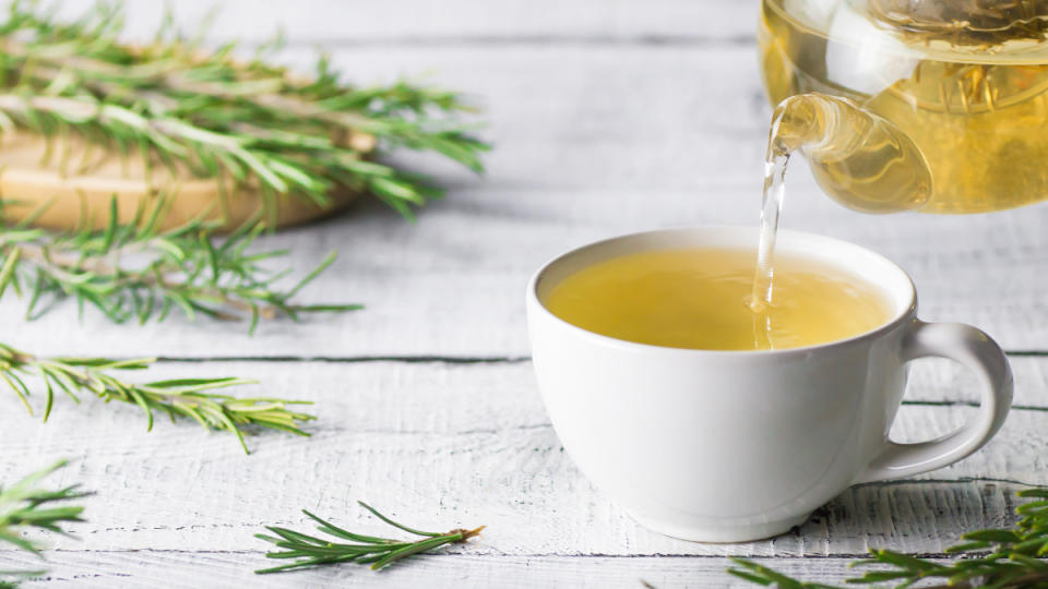 A white cup of rosemary tea beside fresh rosemary