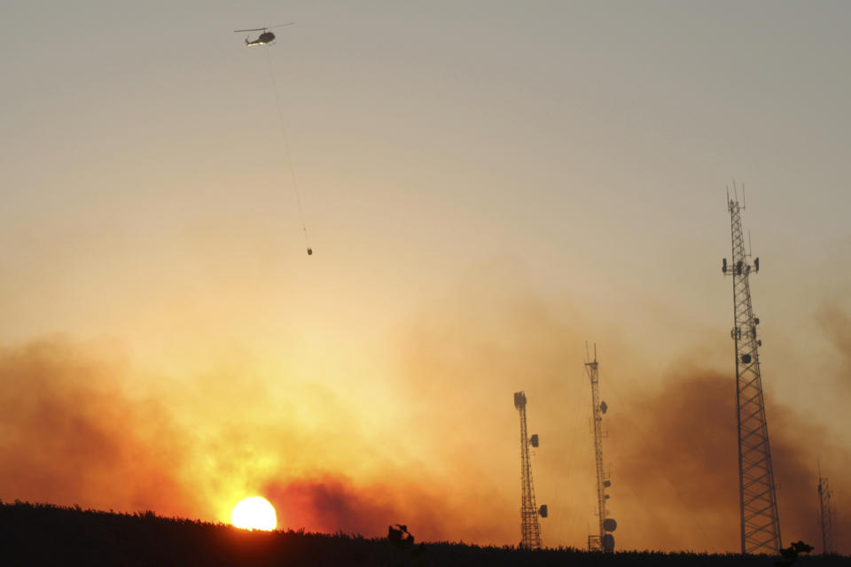 A helicopter carries water on a longline to a wildfire near Salem, Ore., at sunset Friday, Sept. 9, 2022. Climate change is bringing drier conditions to the Pacific Northwest and that requires strategies that have been common in fire-prone California for the past decade or more, said Erica Fleishman, director of the Oregon Climate Change Research Institute at Oregon State University. (AP Photo/Andrew Selsky)