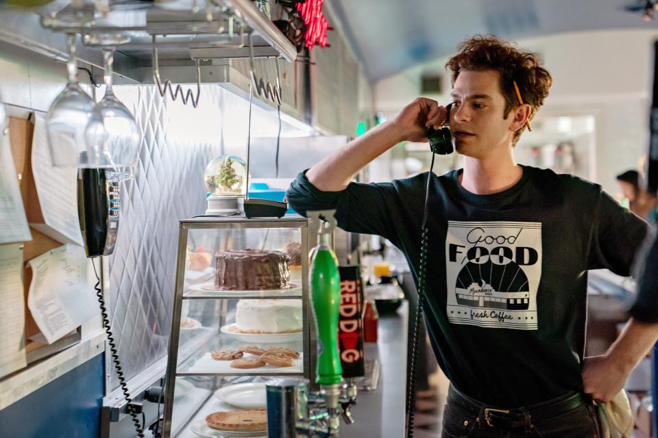 Andrew Garfield stands in a diner talking on the phone