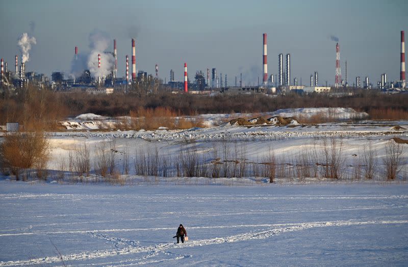 A fisherman walks near an oil refinery in Omsk