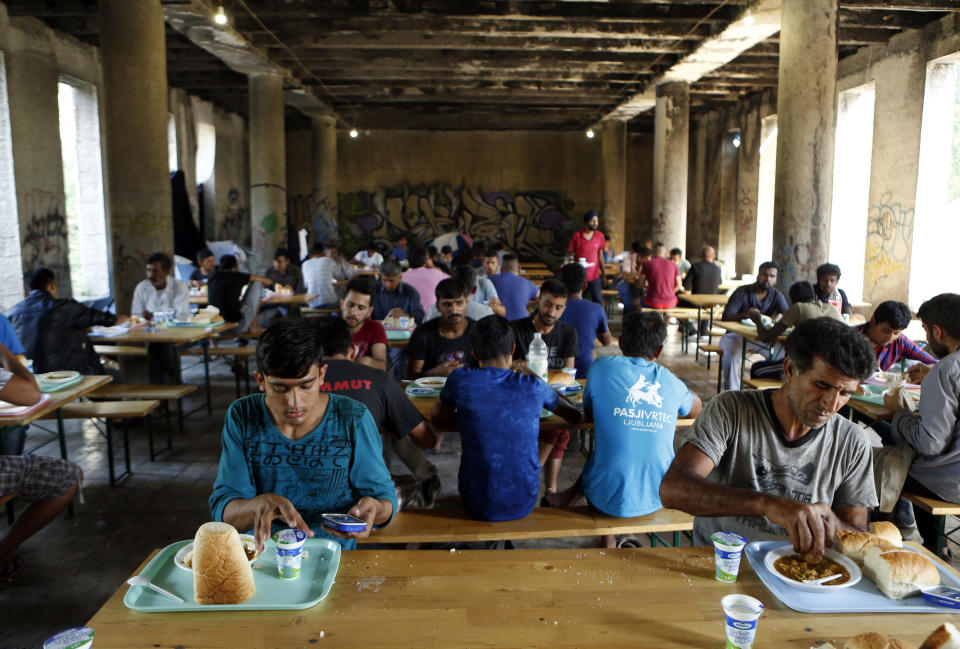 In this photo taken on Monday, Aug. 13, 2018, migrants eat lunch in a makeshift migrant camp in Bihac, 450 kms northwest of Sarajevo, Bosnia. Impoverished Bosnia must race against time to secure proper shelters for at least 4,000 migrants and refugees expected to be stranded in its territory during coming winter. The migrant trail shifted toward Bosnia as other migration routes to Western Europe from the Balkans were closed off over the past year. (AP Photo/Amel Emric)