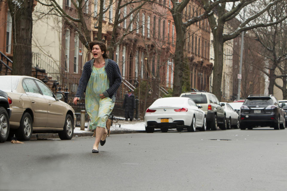 Person in a dress, wearing a striped cardigan and flats, running down a street in a residential area, appearing distressed