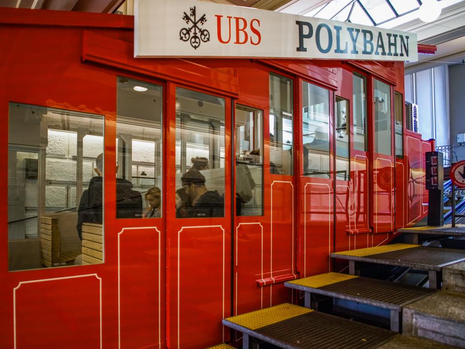 A red elevated railway car, Polybahn, stopped at a station.