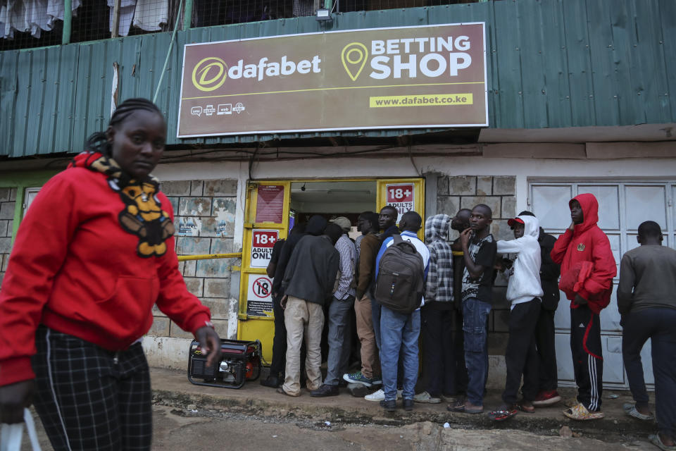 Customers queue outside a sports betting shop in the low-income Kibera neighborhood of the capital Nairobi, Kenya, Monday, Dec. 5, 2022. Although sports betting is a global phenomenon and a legitimate business in many countries, the stakes are high on the continent of 1.3 billion people because of lax or non-existent regulation, poverty and widespread unemployment. (AP Photo/Brian Inganga)