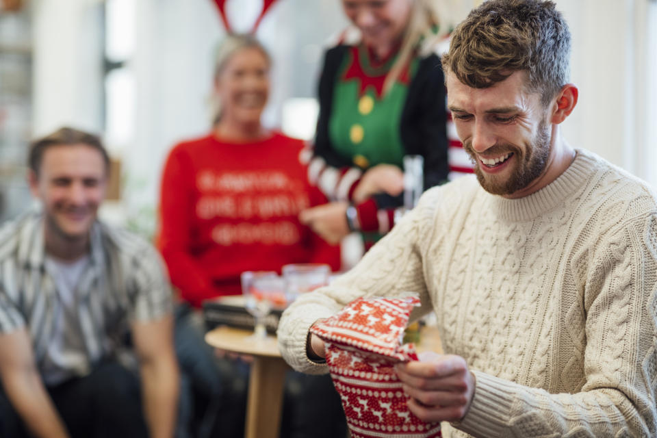 Office staff enjoying a Christmas party together, unwrapping gifts as part of secret Santa. A man is unwrapping a gift while laughing. They are in the North east of England.