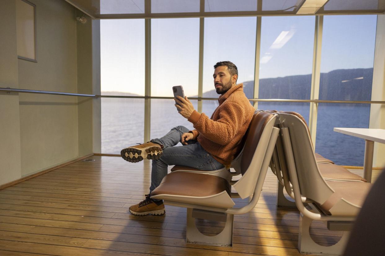 man sitting with his phone in the waiting room to board his trip