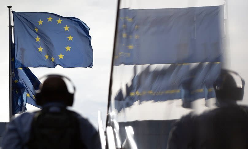 A man wearing headphones walks toward EU flags as he is reflected in the marble of the European Commission building in Brussels, August 2020