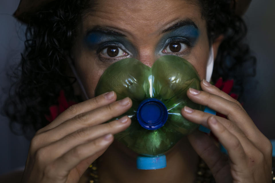 Actress Thais Bezerra puts on a mask made from a plastic bottle as she gets dressed in her costume to perform in a video recording of "Giant Dreamers" outside the Museum of Modern Art (MAM) during the COVID-19 pandemic in Rio de Janeiro, Brazil, Tuesday, March 9, 2021. Brazil’s Congress approved in 2020 a financial lifeline for artists, as well as to maintain cultural venues and small troupes that had to cease activities. (AP Photo/Bruna Prado)