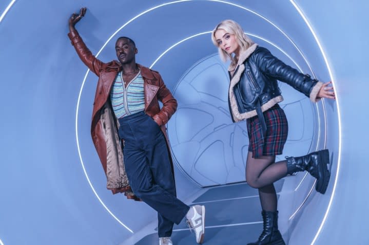 Doctor Who stars Ncuti Gatwa and Millie Gibson pose near a futuristic door.