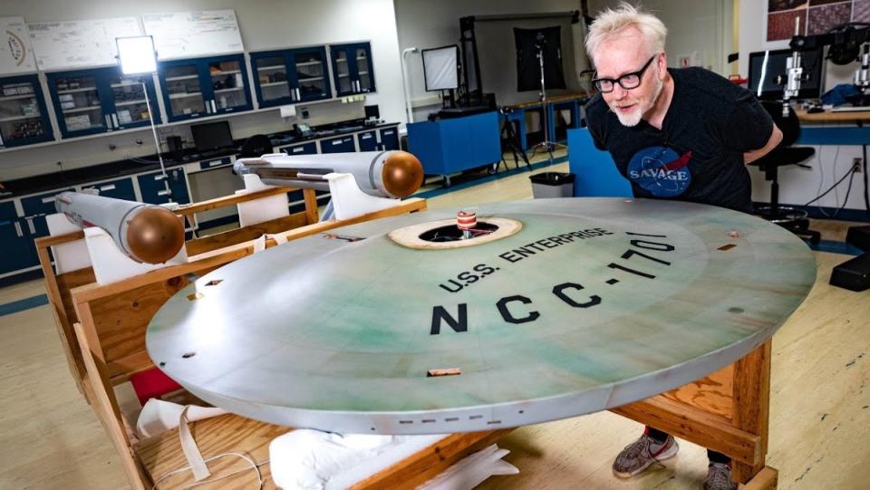 Adam Savage leans over the model of the U.S.S. Enterprise from Star Trek at the Smithsonian Air and Space Museum