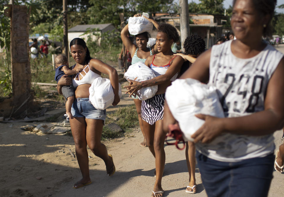 Women carry home bags of donated food, distributed by the the Covid Without Hunger organization in the Jardim Gramacho slum of Rio de Janeiro, Brazil, Saturday, May 22, 2021. Food insecurity for people with informal jobs is quadruple that of salaried employees, according to Tereza Campello, a former minister of social development. (AP Photo/Silvia Izquierdo)