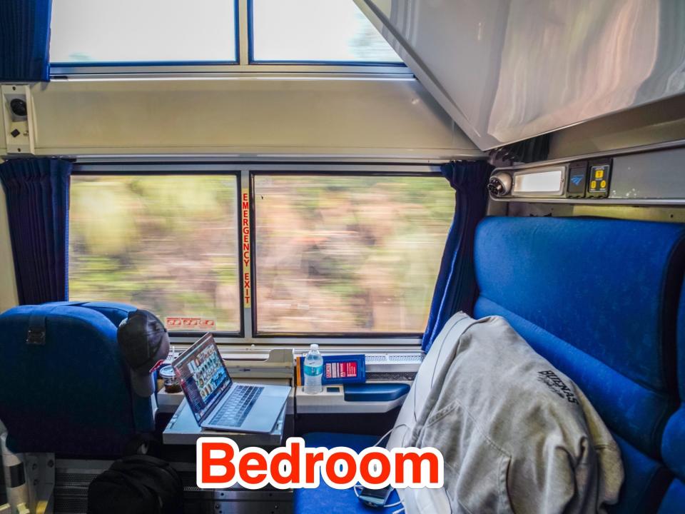 Inside an Amtrak bedroom with blue seats and a big window showing nature outside