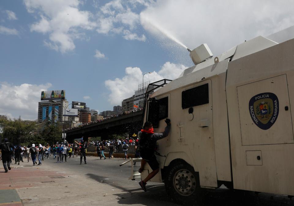 <p>Un manifestante se aferra a un vehículo policial que dispara agua a presión al resto de los protestantes Caracas, Venezuela April 6, 2017. REUTERS/Carlos Garcia Rawlins</p>