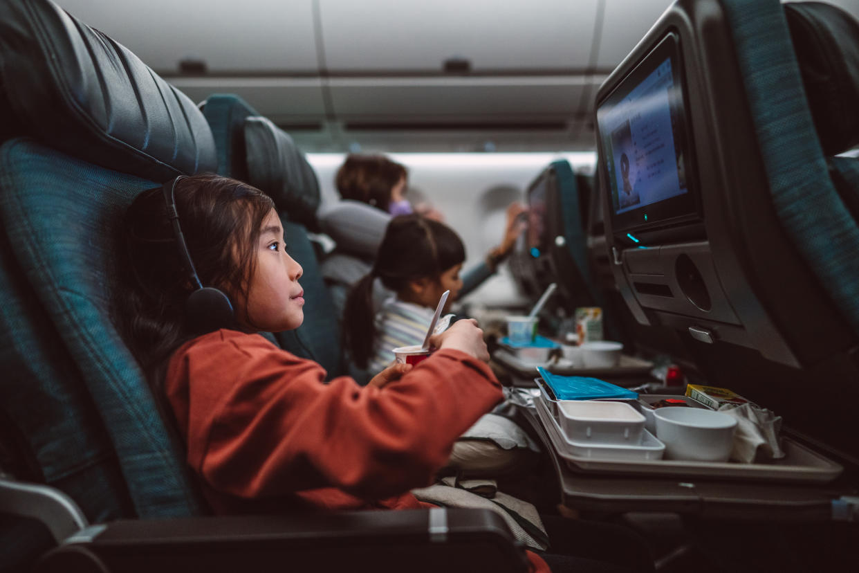 Little girl watching movie on the seat-back TV screen while enjoying her airline meal during travel with family.