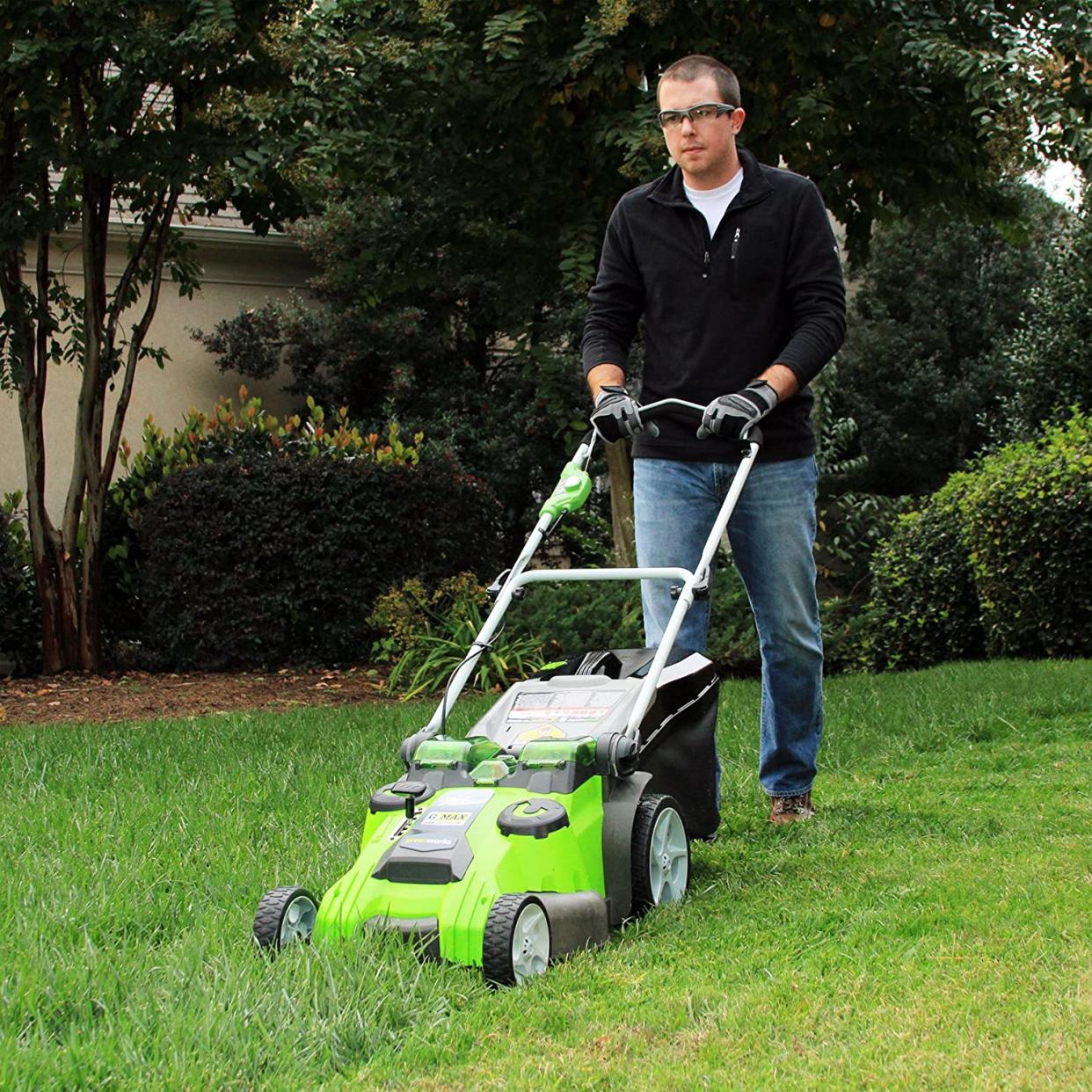 Man wearing safety glasses and gloves while mowing lawn with push mower