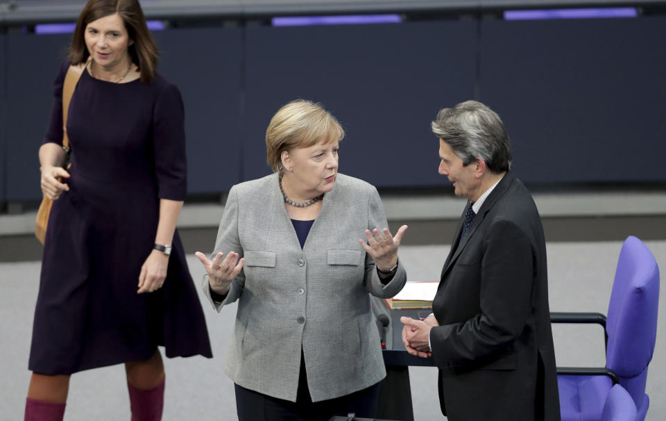 Green party co-faction leader Katrin Goering-Eckardt, left, walks past German Chancellor Angela Merkel, center, as Merkel talks to the faction leader of the German Social Democrats, Rolf Mützenich, right, prior to a meeting of the German parliament, Bundestag, at the Reichstag building in Berlin, Germany, Wednesday, Dec. 18, 2019. (AP Photo/Michael Sohn)