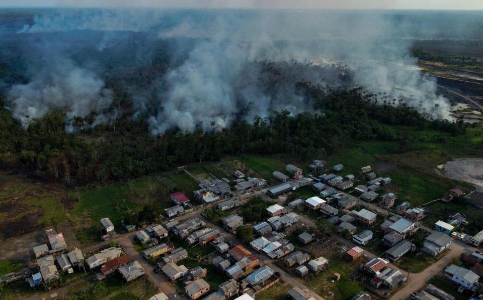 The smoke from a fire in a forest area approaches houses at the Cacau Pirera District in Iranduba, Amazonas state, Brazil