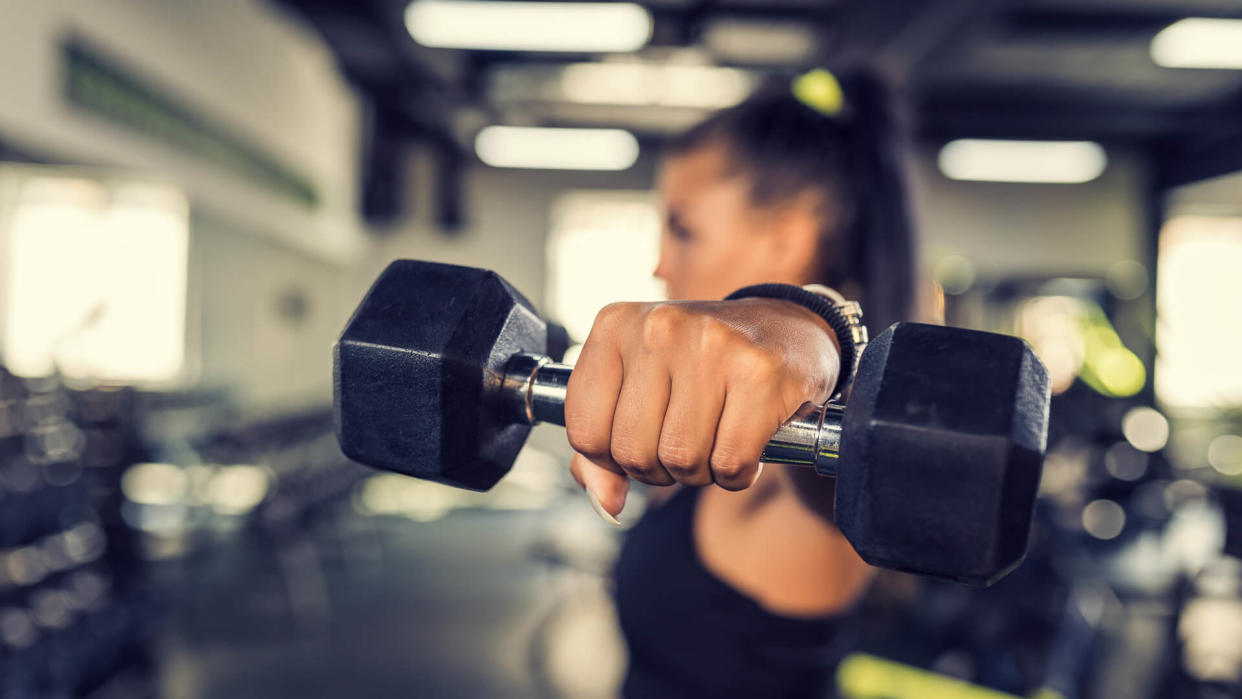 Young woman doing shoulder exercise using dumbbells.