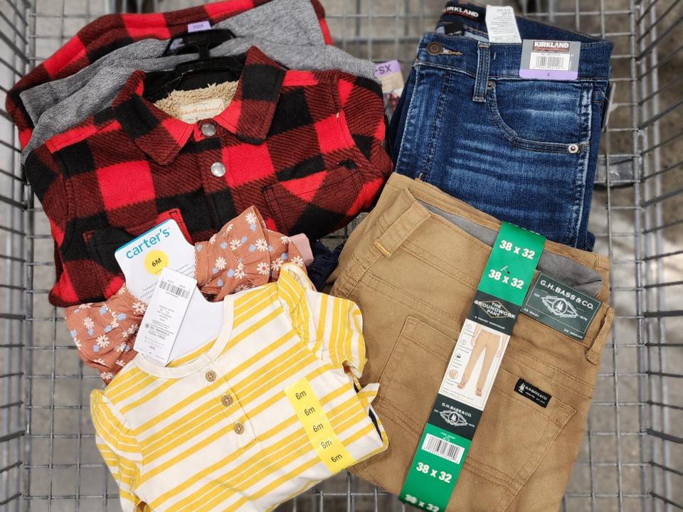 A buffalo-plaid shirt, a yellow-striped shirt, denim jeans, khaki pants, and some clothes stacked underneath in a shopping cart