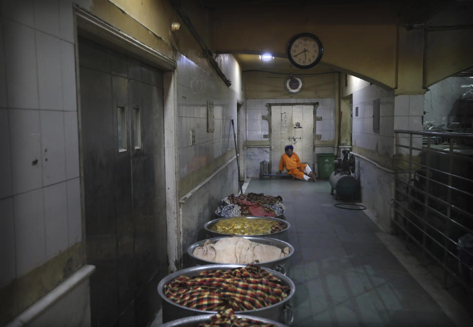 A Sikh cook rests as large vessels containing cooked rice lie covered with cloth in the kitchen hall of the Bangla Sahib Gurdwara in New Delhi, India, Sunday, May 10, 2020. The Bangla Sahib Gurdwara has remained open through wars and plagues, serving thousands of people simple vegetarian food. During India's ongoing coronavirus lockdown about four dozen men have kept the temple's kitchen open, cooking up to 100,000 meals a day that the New Delhi government distributes at shelters and drop-off points throughout the city. (AP Photo/Manish Swarup)