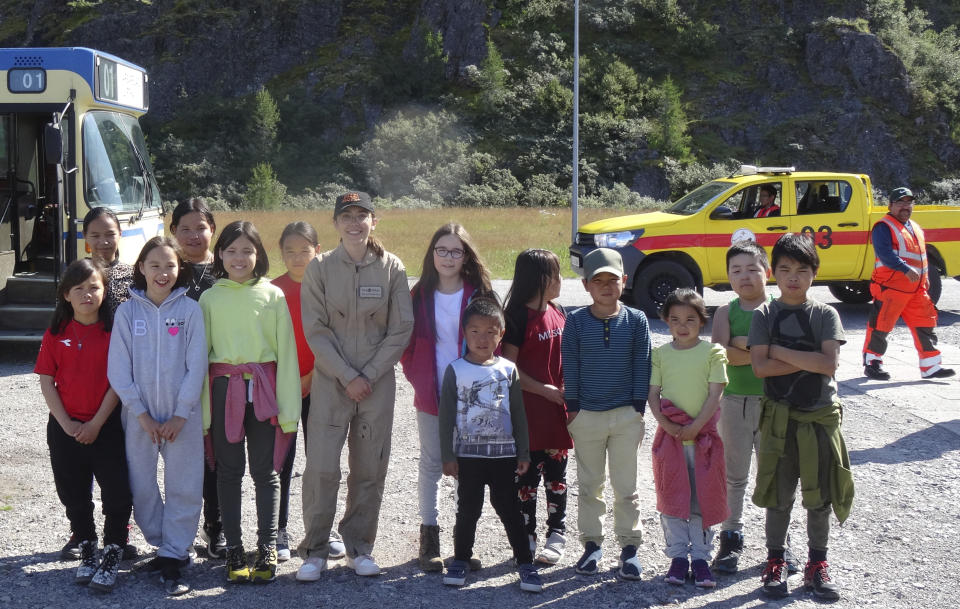 In this undated photo provided by FlyZolo, Zara Rutherford, seventh left, poses with local children as she arrives in Greenland. Zara Rutherford is set to land in Kortrijk, Belgium on Monday, Jan. 17, 2022, in the hopes of completing her trek around the world as the youngest woman ever, beating the mark of American aviator Shaesta Waiz, who was 30 when she set the previous benchmark.(FlyZolo via AP)