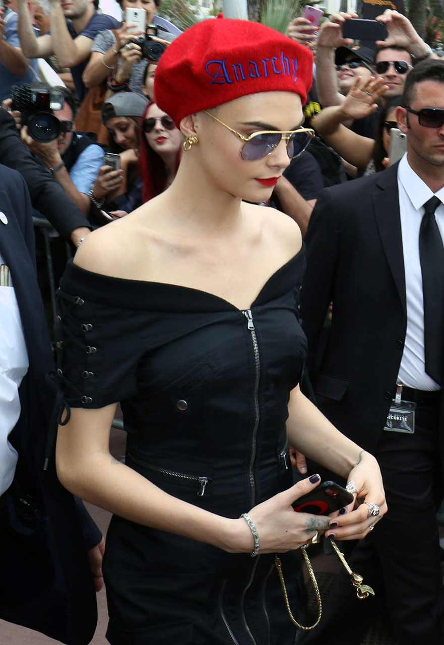 <p>At the Cannes Film Festival in France, Cara Delevingne, who recently shaved her head for a role in a movie, wore a red beret with the word “Anarchy” stitched on it. She paired it with a black off-the-shoulder dress, aviator sunglasses, and matched her bright red lips to her hat. (Photo: Splash) </p>