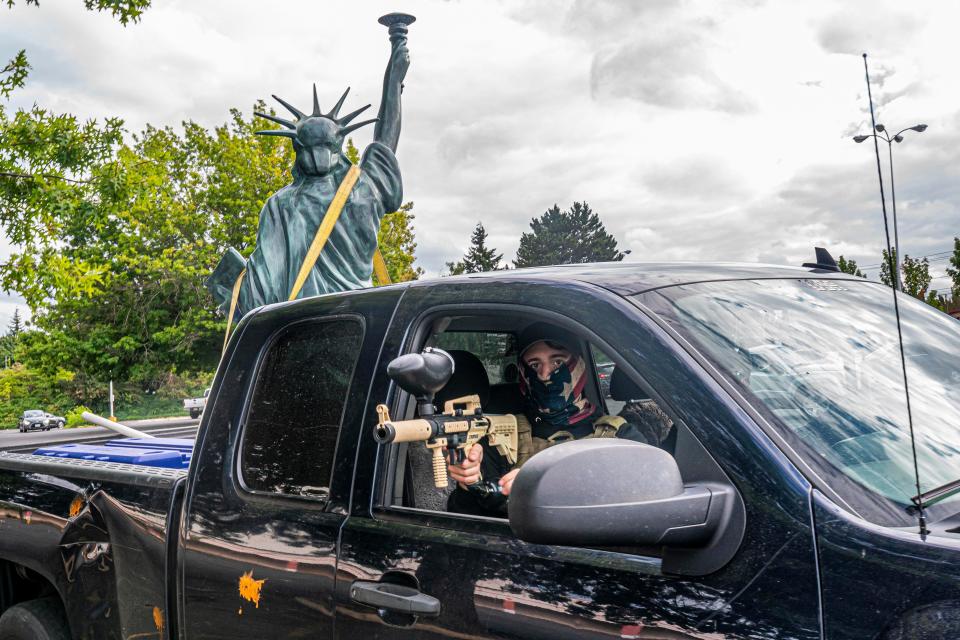 A member of the far-right Proud Boys group aims a paintball gun while leaving a demonstration with a Statue of Liberty replica in the bed of the truck on Aug. 22 in Portland, Ore. The Proud Boys and other far-right extremists fought with left-wing activists.