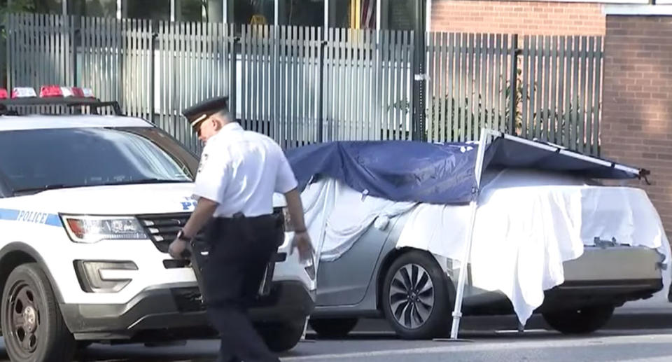 A police officer walks past a car covered in sheets as a crime scene is erected in the Bronx. Two babies died in the car after their dad left them inside for about eight hours while he worked.