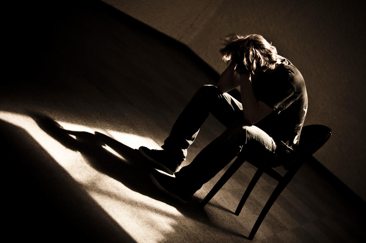 A photo illustration of a man sitting in a chair in a dark room looking down with his head in his hands.