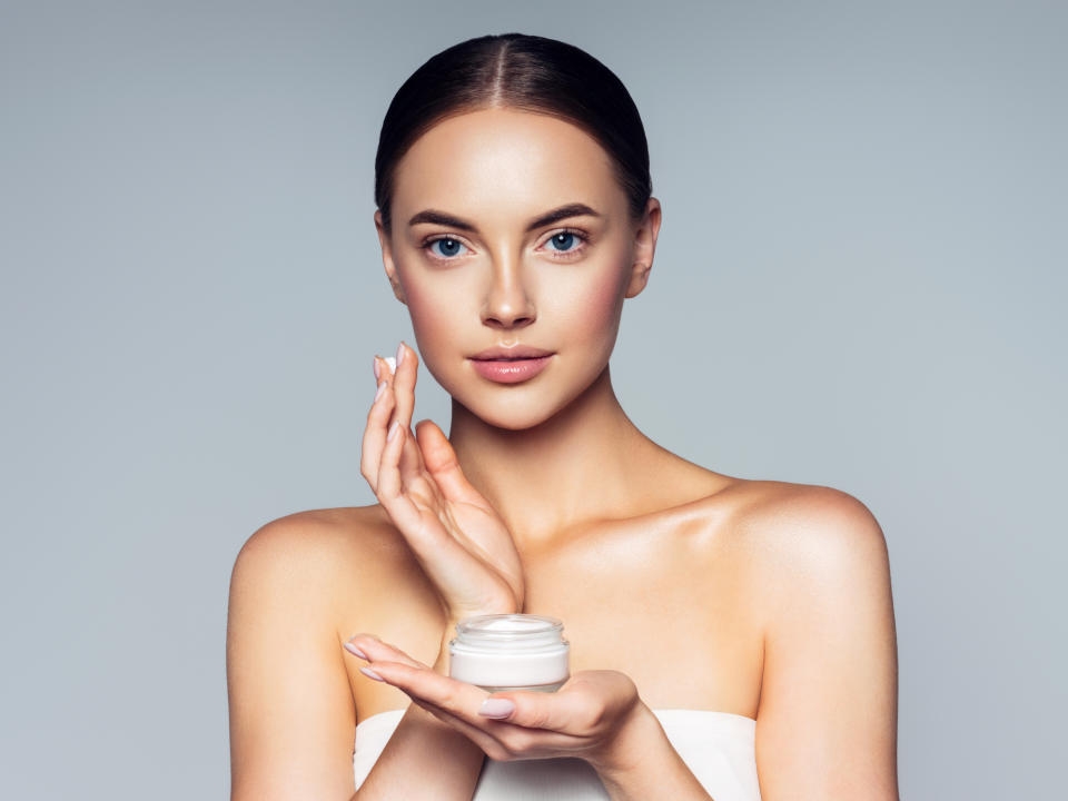 Woman holding a skincare product, looking at the camera for a promotional shot