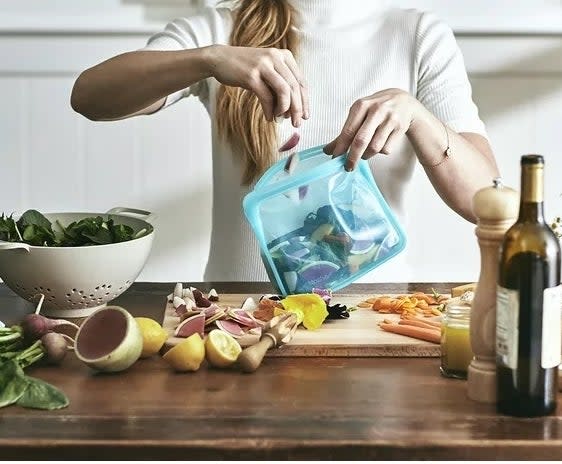 model putting vegetables in a green stasher bag