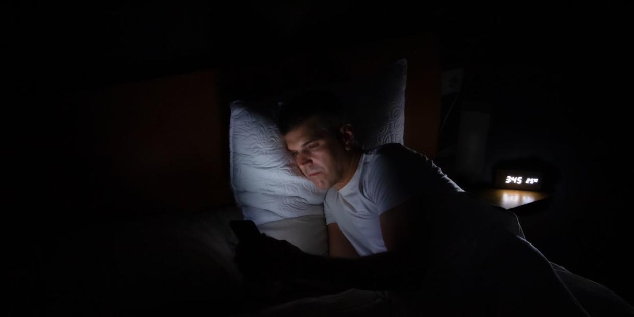 a man is lying in bed in total darkness looking at his smart phone