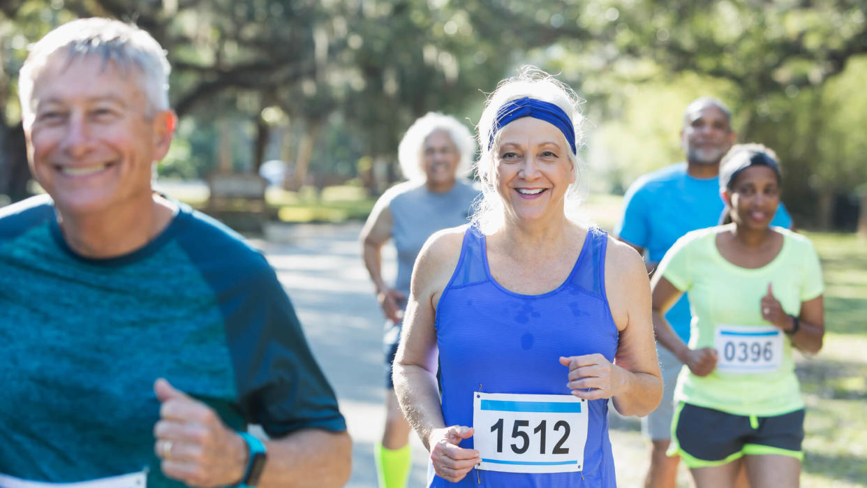 A group of five multi-ethnic seniors running in a race, wearing marathon bibs.