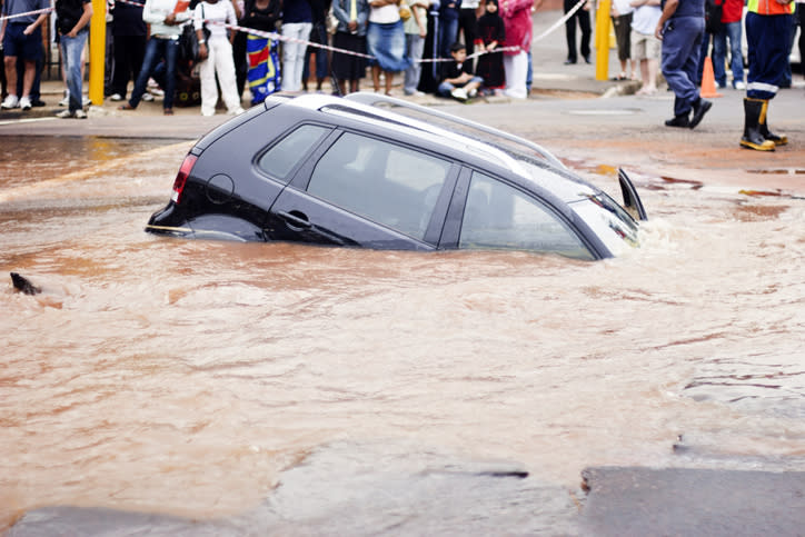 Car submerged in water with onlookers and a rescue worker nearby