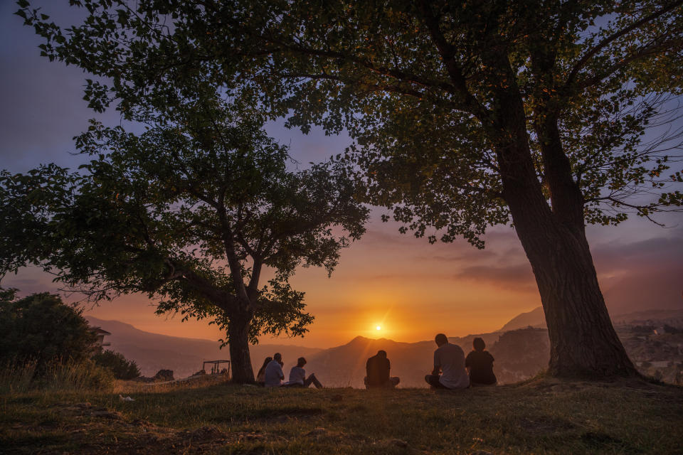 People sit and reflect as the sun sets over the scenic Kadisha Valley, a holy landmark for Lebanon's Maronite Christians, in the northeast mountain town of Bcharre, Lebanon, Friday, July 21, 2023. For Lebanon's Christians, the cedars are sacred, these tough evergreen trees that survive the mountain's harsh snowy winters. They point out with pride that Lebanon's cedars are mentioned 103 times in the Bible. (AP Photo/Hassan Ammar)