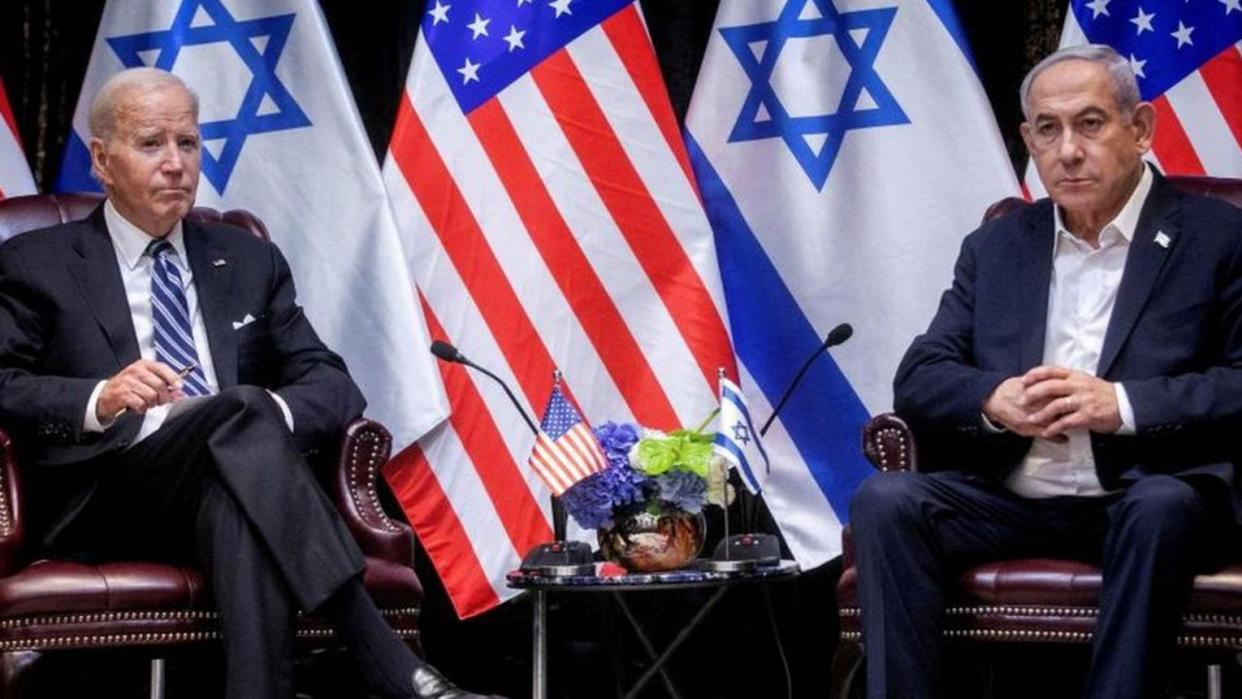Biden y Netanyahu, sentados junto a una mesa, con las banderas de sus países detrás. 