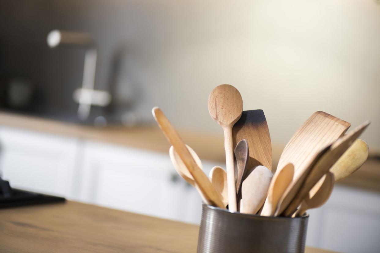 Close-up of wooden spoons and spatulas in holder on kitchen worktop.