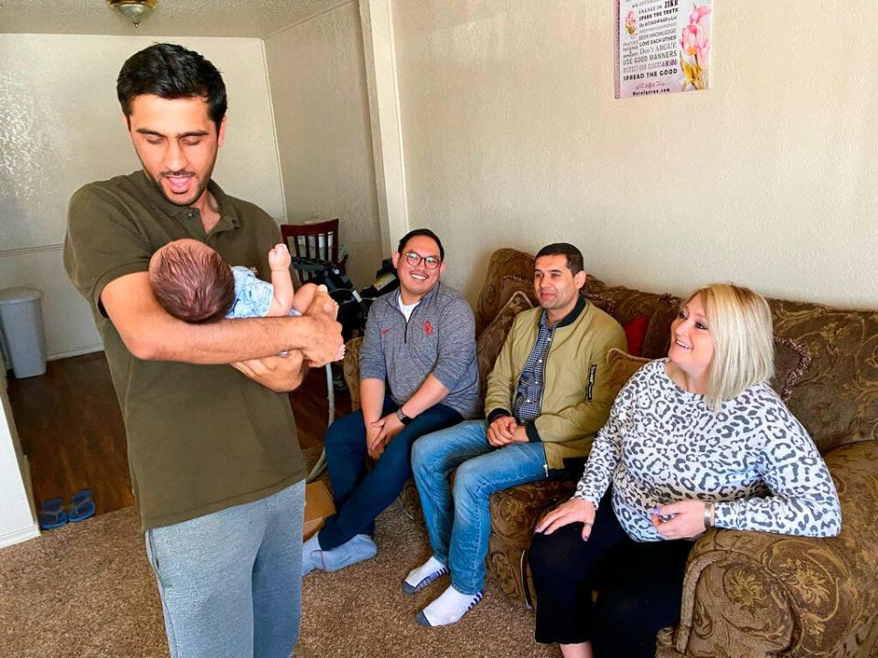 Afghan refugee Shirkhan Nejat, left, talks to his 2-month-old son, Ansar, at the family's Oklahoma City apartment on Saturday, April 2, 2022. In the background are Joseph Pham, left, a refugee case manager for Catholic Charities of Oklahoma City; a translator, center; and Carly Akard, director of communications for Catholic Charities.