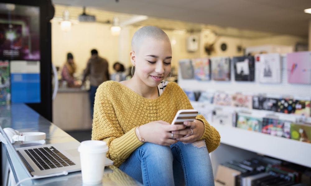 Teenage girl with shaved head with cell phone in cafe