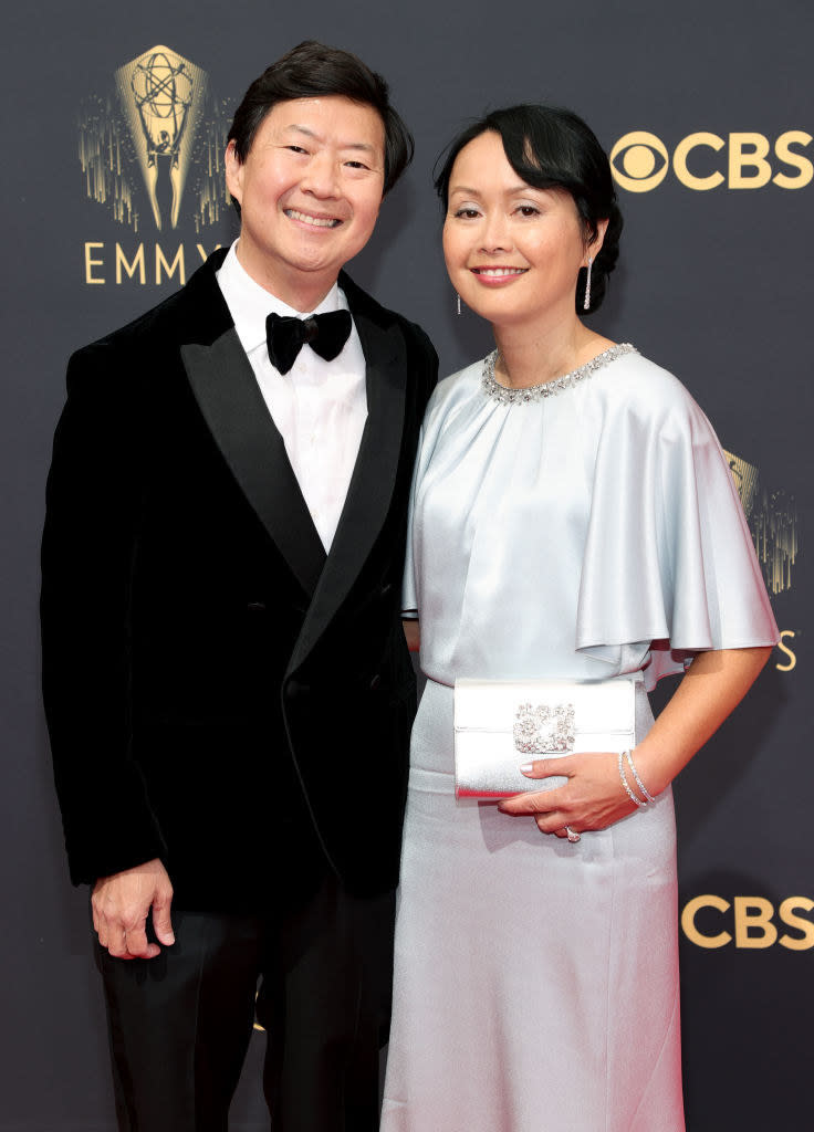 Ken Jeong wears a dark suit and Tran Jeong shiny gown with oversized short sleeves